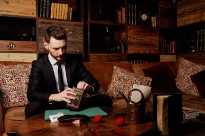 Un homme en costume, les mains levées, portant un masque noir sur les yeux dans un environnement sombre.