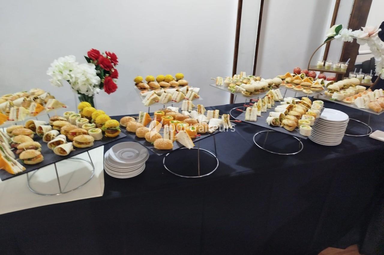 Buffet avec une variété de bouchées salées, sandwichs et fleurs décoratives sur une nappe noire.
