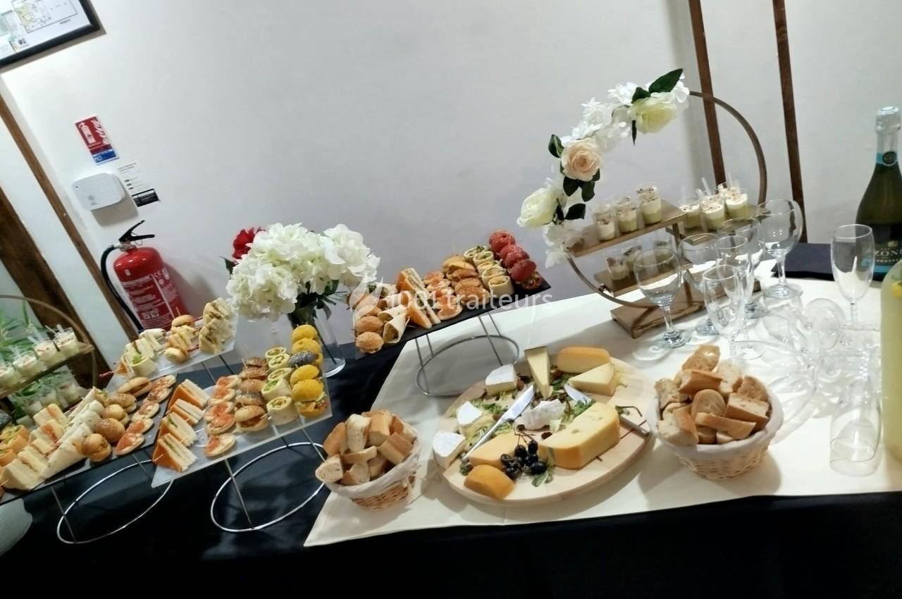 Buffet avec assortiment de fromages, pains, verrines, amuse-bouches et décorations florales sur une table.