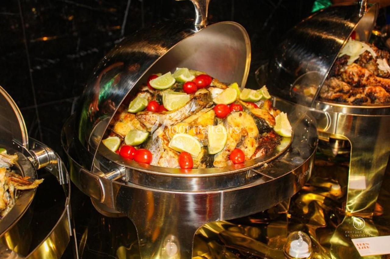 Plat de buffet en inox contenant des morceaux de poisson grillé garnis de quartiers de citron et de tomates cerises.