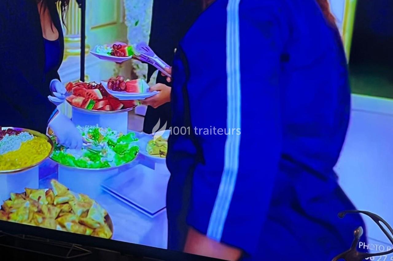 Personnes se servant à un buffet comprenant des salades, fruits et samoussas, avec des plats disposés sur une table.