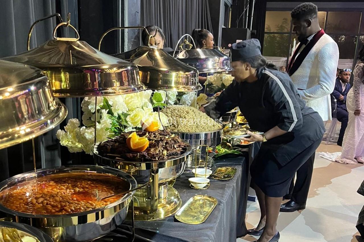Buffet avec plats variés, une femme en tenue de service sert des invités dans un cadre élégant avec décoration florale.