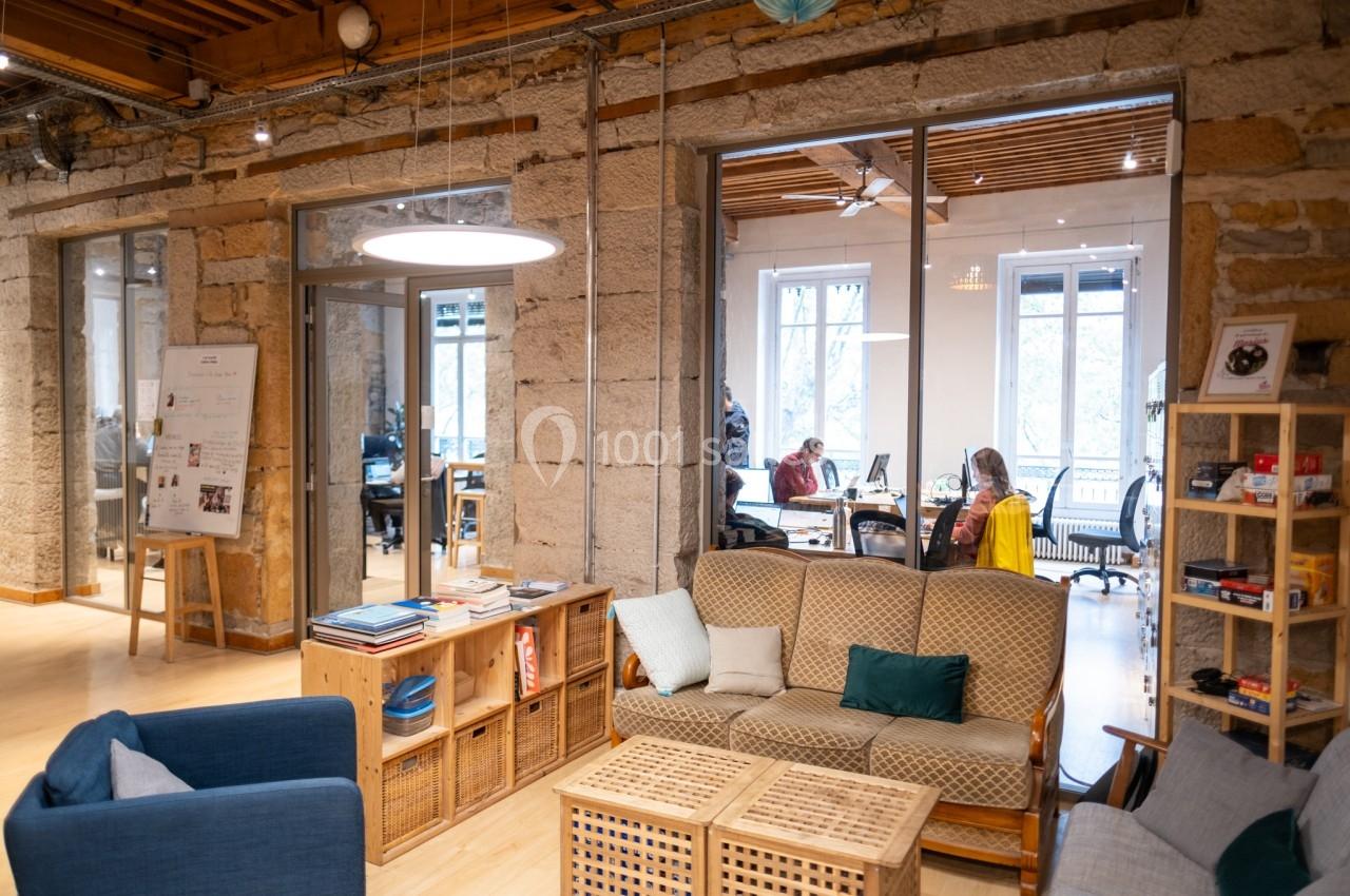 Espace de coworking lumineux avec canapés, étagères et vue sur une salle de travail vitrée en arrière-plan.