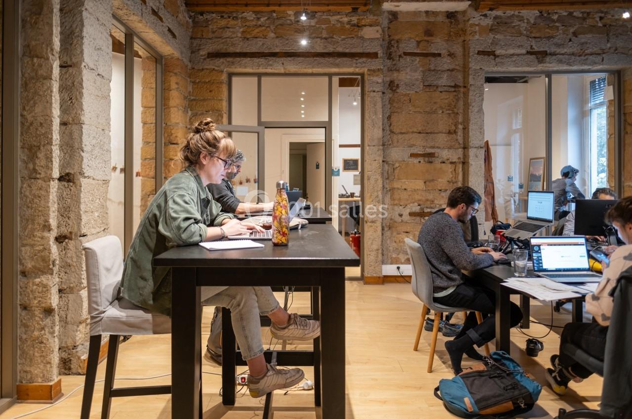 Personnes travaillant sur des ordinateurs dans un espace de coworking avec murs en pierre et mobilier moderne.