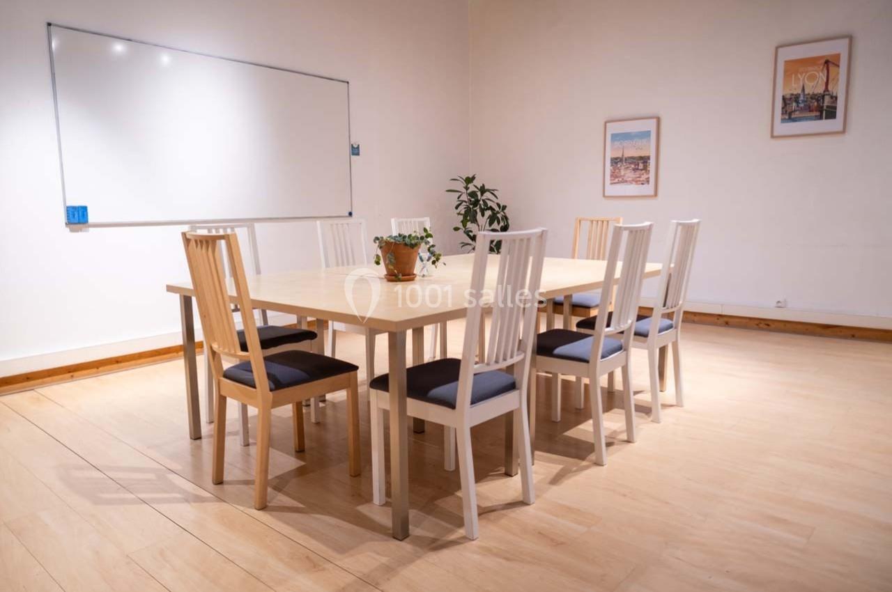 Salle de réunion lumineuse avec une grande table en bois entourée de chaises et un tableau blanc au mur.