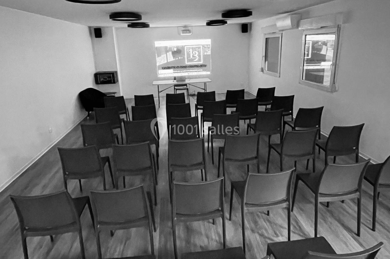 Salle de réunion avec des rangées de chaises vides face à un écran de projection allumé.