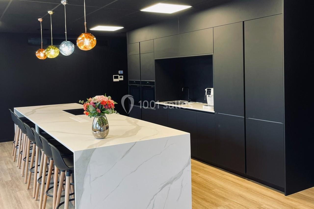 Cuisine moderne avec un îlot central en marbre blanc, chaises hautes, luminaires colorés et armoires noires intégrées.
