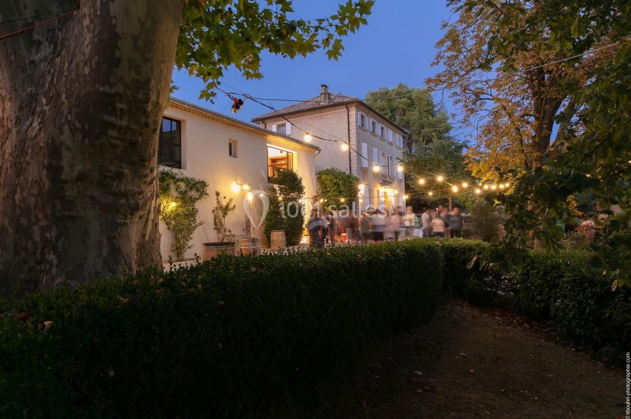 Façade d'une maison éclairée par des guirlandes lumineuses, entourée de végétation au crépuscule.
