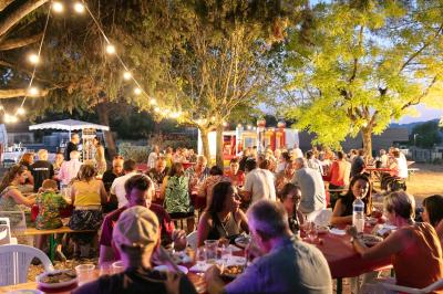 Une main verse du vin blanc dans un verre transparent, avec des bouteilles en arrière-plan flou.