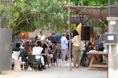 Une main verse du vin blanc dans un verre transparent, avec des bouteilles en arrière-plan flou.