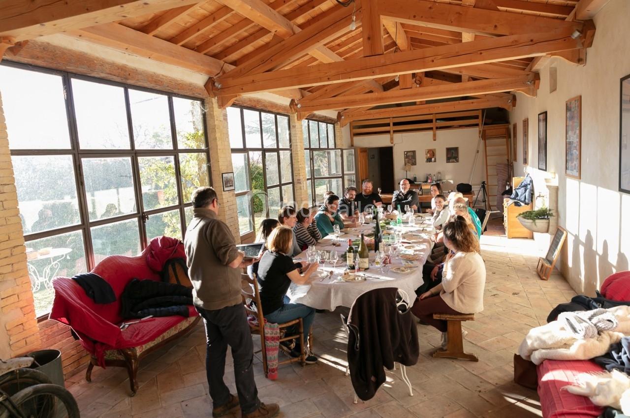 Un groupe de personnes partage un repas autour d'une grande table dans une pièce lumineuse avec des murs vitrés.