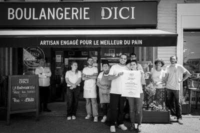 Une main verse du vin blanc dans un verre transparent, avec des bouteilles en arrière-plan flou.