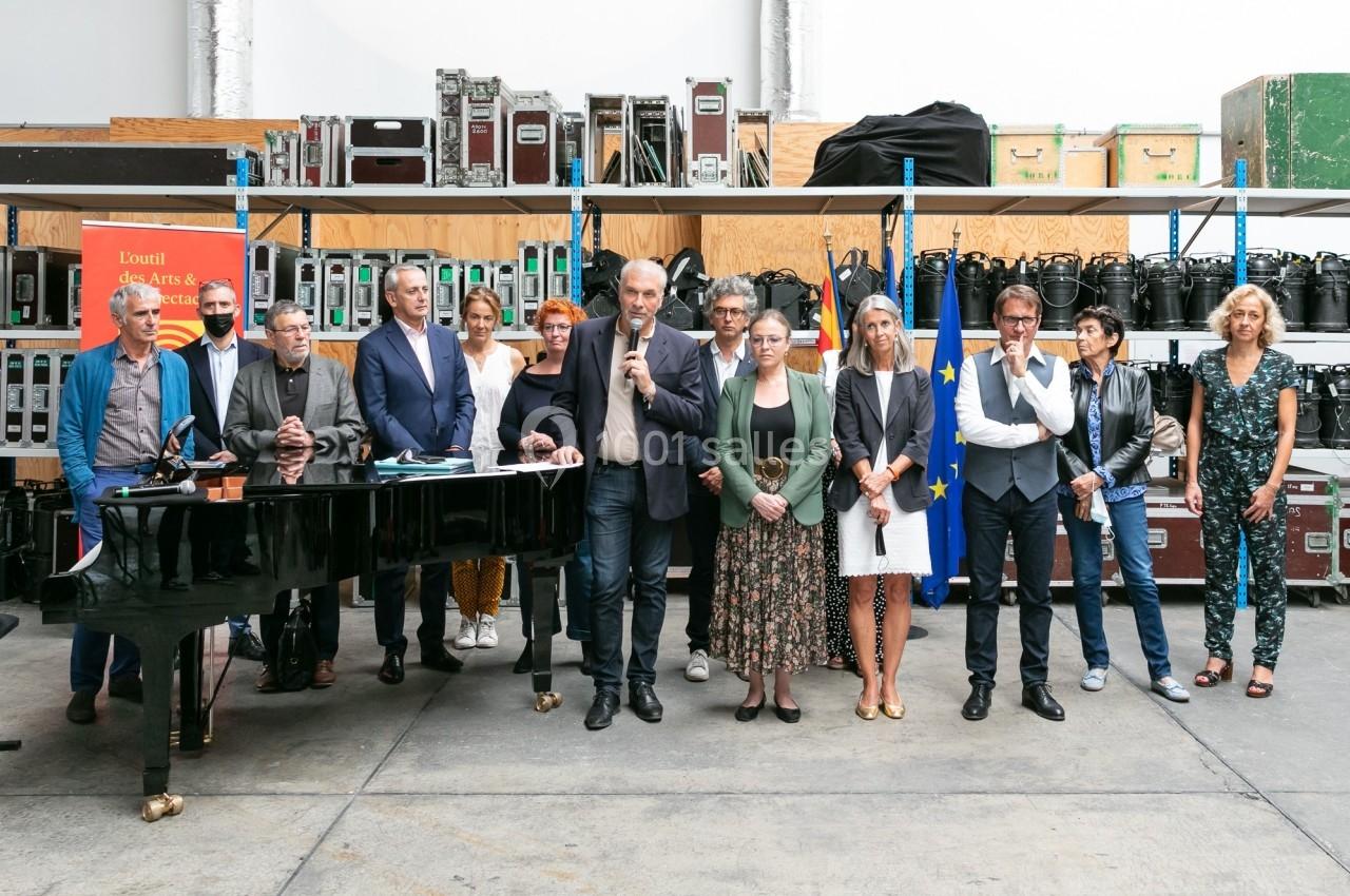 Un groupe de personnes debout dans un espace industriel, avec un piano à queue et des équipements en arrière-plan.