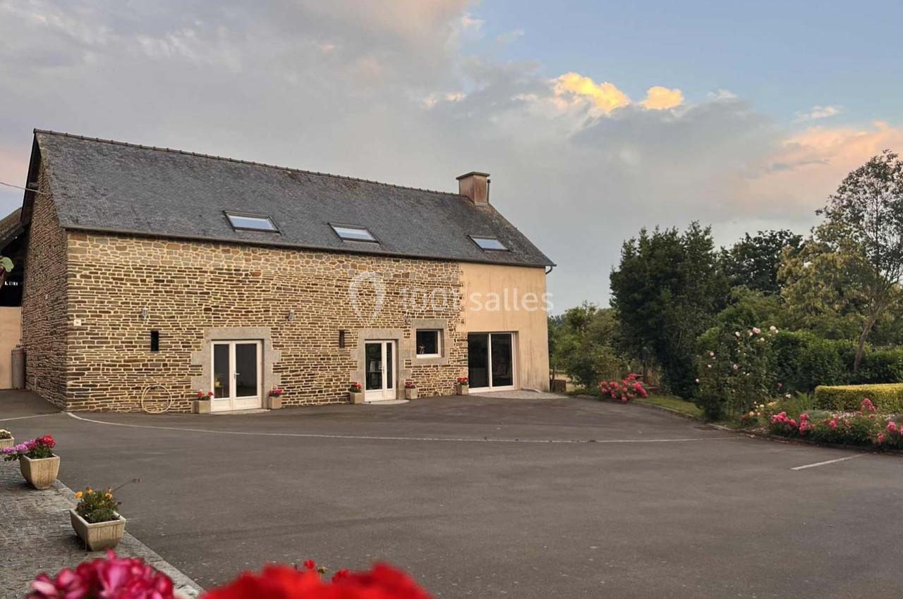 Façade d'une maison en pierre et crépi avec un toit en ardoise, entourée de fleurs et d'un espace pavé.