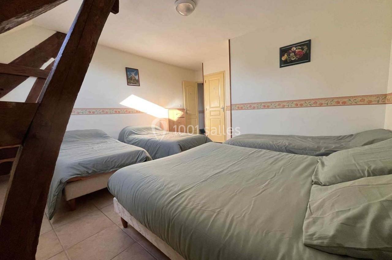 Chambre lumineuse avec trois lits simples, murs blancs décorés de cadres et une porte en bois clair.
