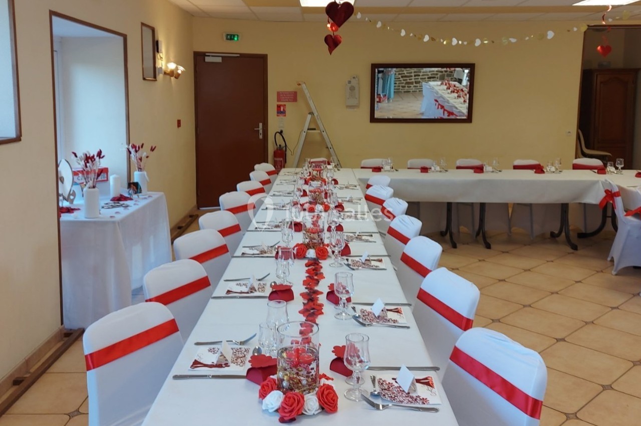 Salle décorée pour un événement avec des tables alignées, nappes blanches et accents rouges, chaises assorties.