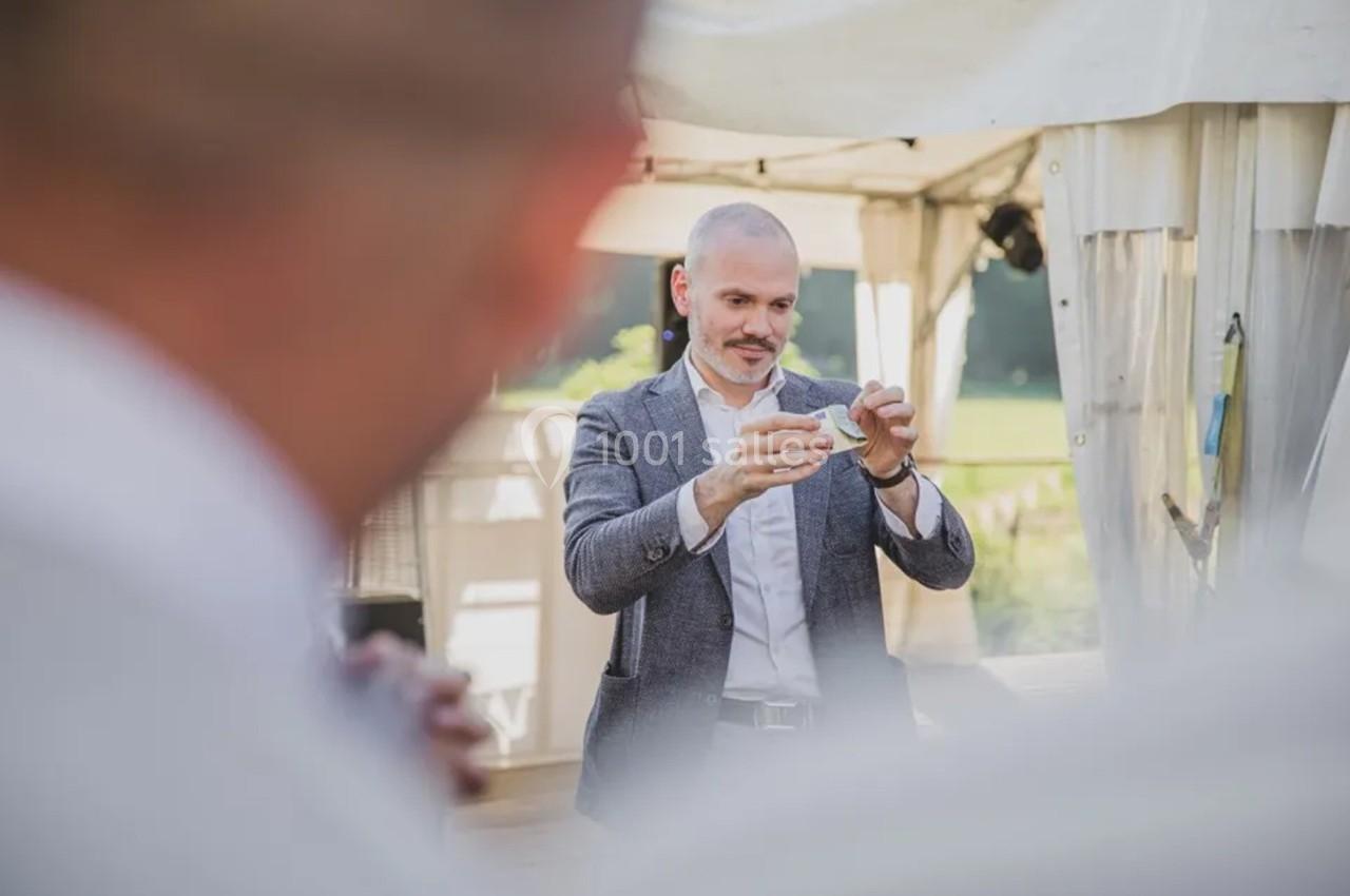 Un homme en costume réalise un tour de magie en plein air sous une tente blanche.
