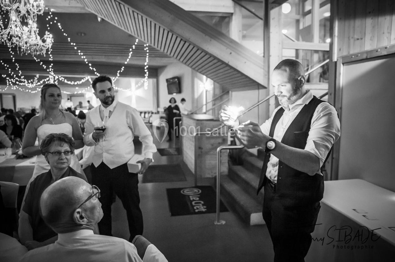 Un homme réalise un tour de magie avec une lumière devant un petit groupe de personnes dans une salle de réception.