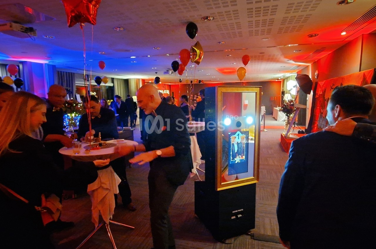Des personnes participent à un événement festif en intérieur, avec des ballons et un photobooth lumineux.