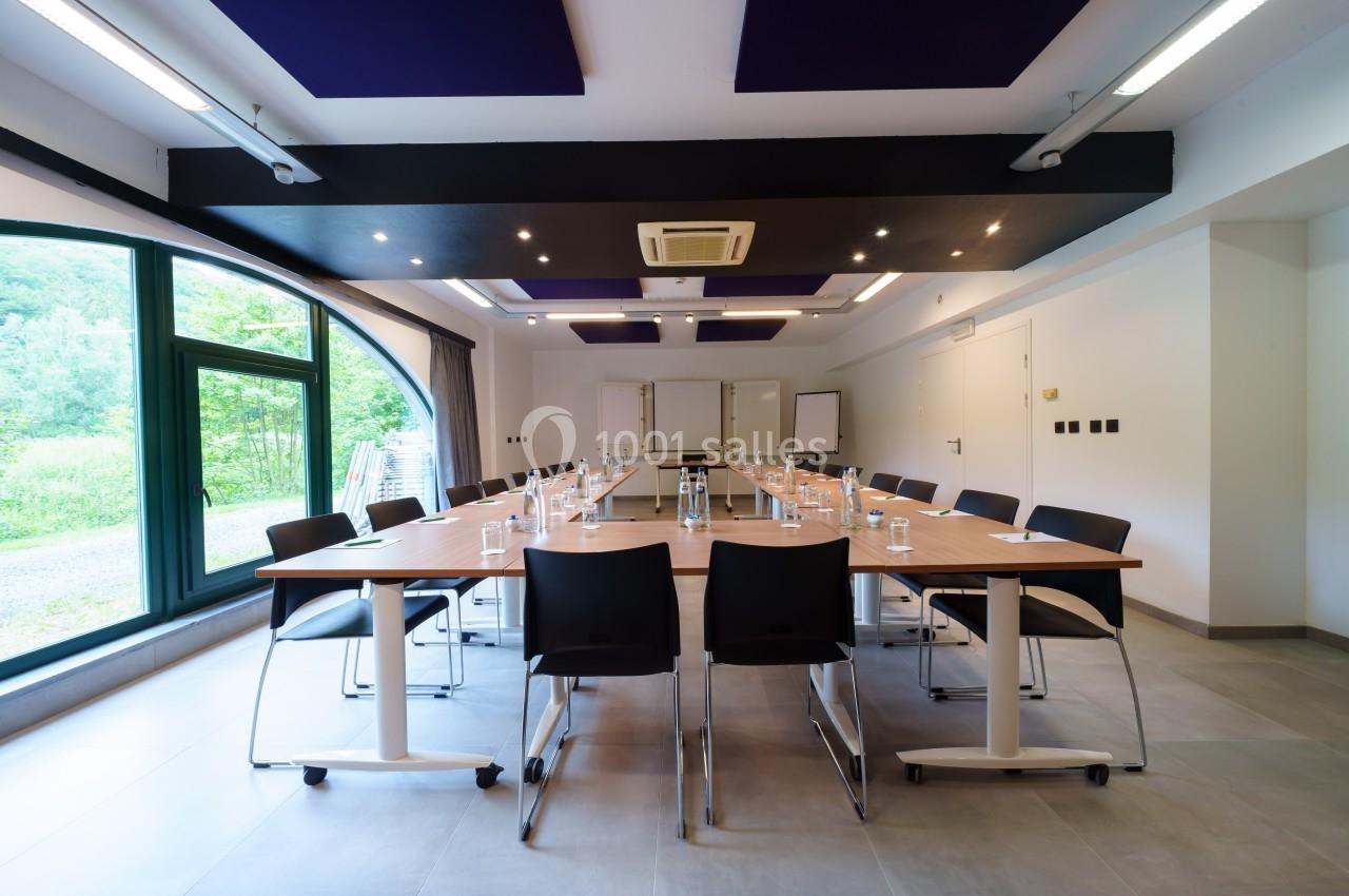 Salle de réunion lumineuse avec une grande table en U, des chaises noires et une vue sur l'extérieur verdoyant.