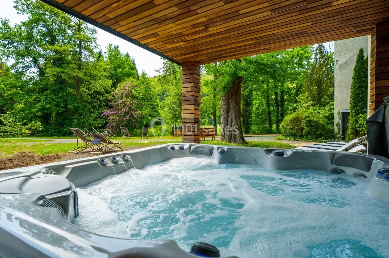 Bain à remous extérieur sous un abri en bois, entouré de verdure et de chaises longues dans un cadre naturel.