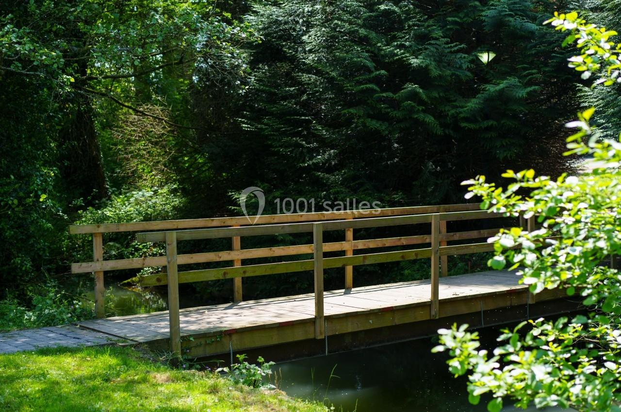 Passerelle en bois traversant un petit cours d'eau, entourée de végétation dense et d'arbres.