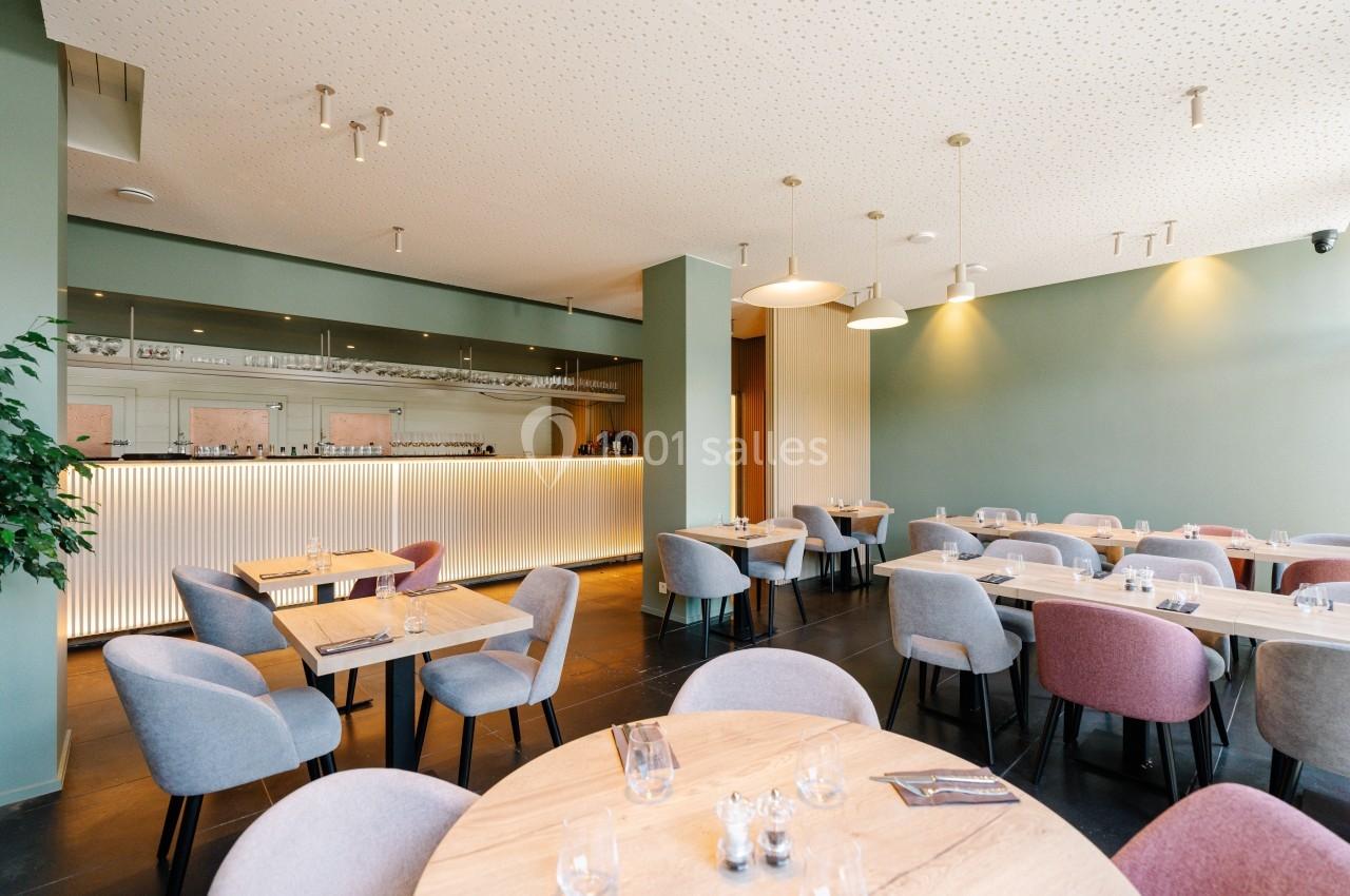 Salle de restaurant moderne avec tables en bois, chaises colorées et bar éclairé en arrière-plan.