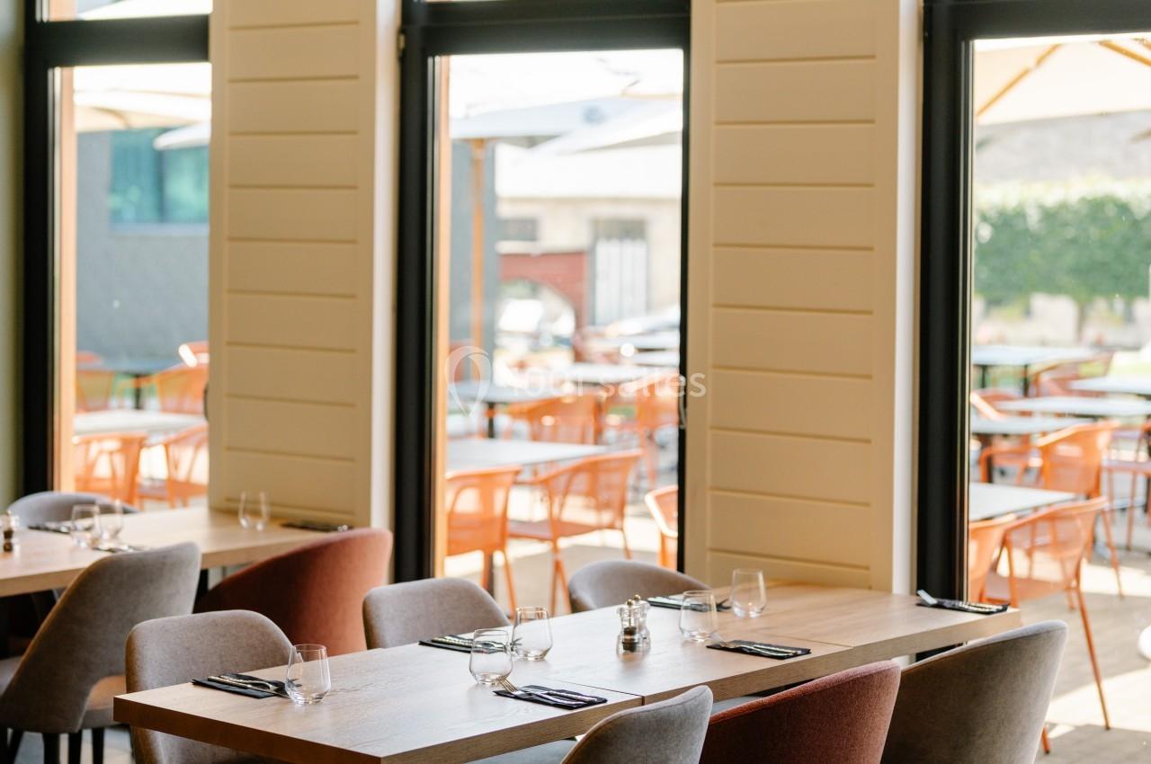 Salle de restaurant lumineuse avec des tables dressées, des chaises colorées et vue sur une terrasse extérieure.