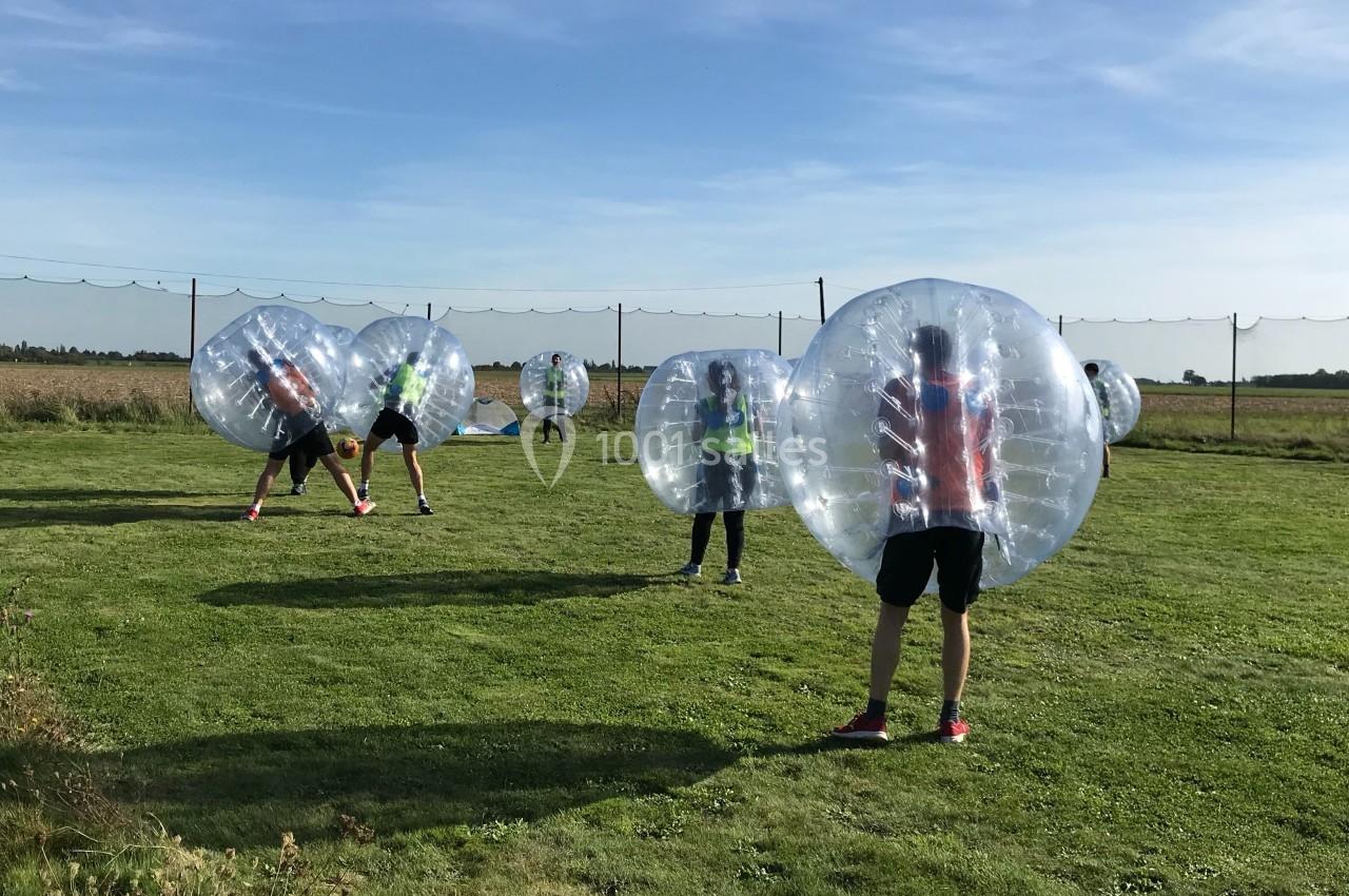 Des personnes jouent au bubble football sur une pelouse, protégées par de grandes bulles gonflables transparentes.