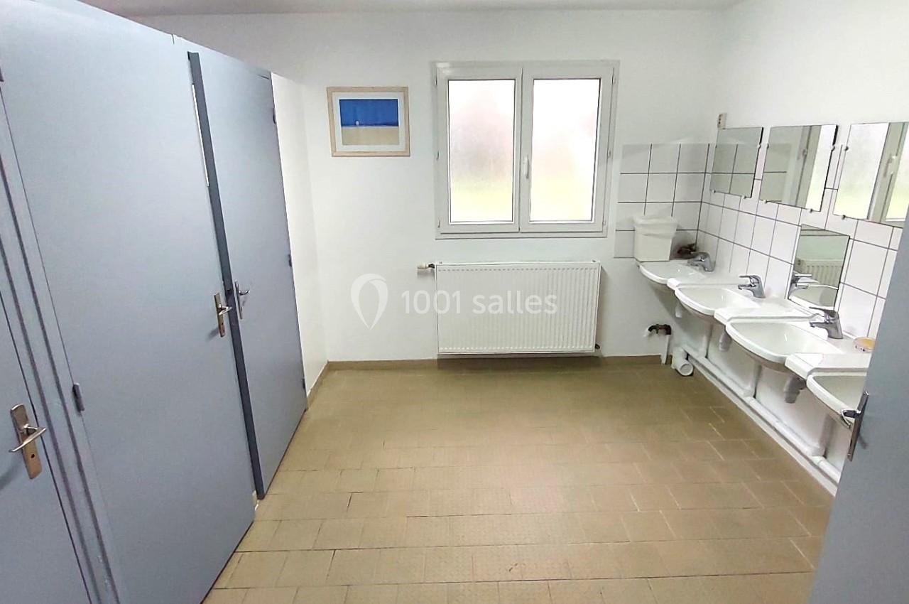 Toilettes pour hommes avec cabines fermées, lavabos alignés et miroir, dans une pièce lumineuse.