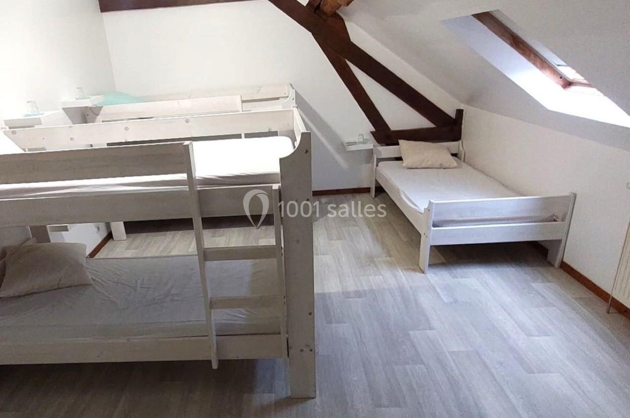 Chambre mansardée avec lits superposés en bois blanc, un lit simple, parquet clair et poutres apparentes.