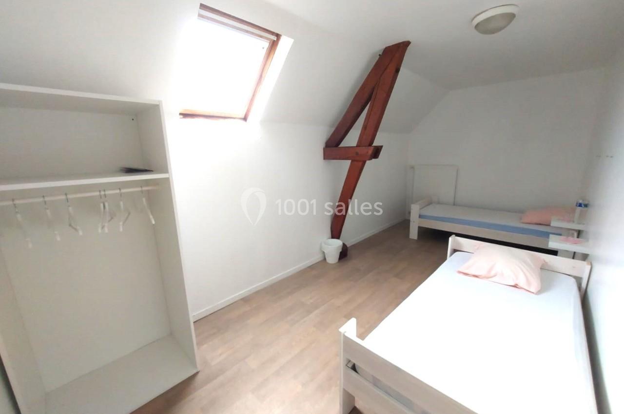 Chambre mansardée avec deux lits simples, un placard ouvert, un mur blanc et une fenêtre de toit apportant de la lumière.