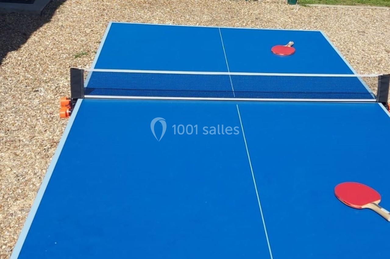 Table de ping-pong bleue en extérieur avec deux raquettes rouges posées de part et d'autre du filet.