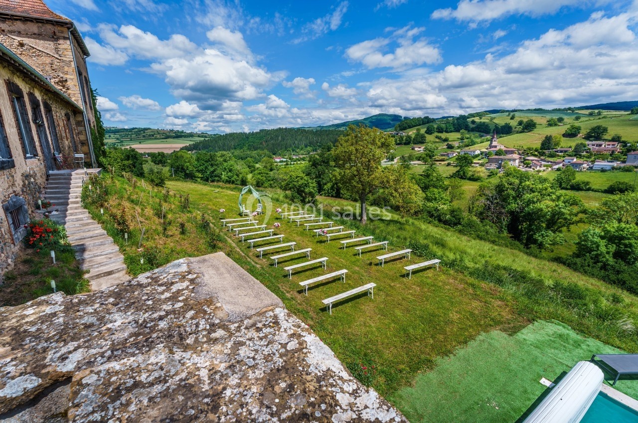 Vue d'un espace extérieur aménagé avec des bancs pour une cérémonie, entouré de verdure et d'un paysage vallonné.
