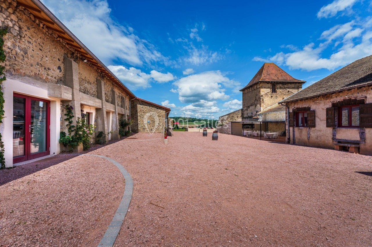 Cour pavée entourée de bâtiments en pierre avec un ciel bleu et des nuages en arrière-plan.