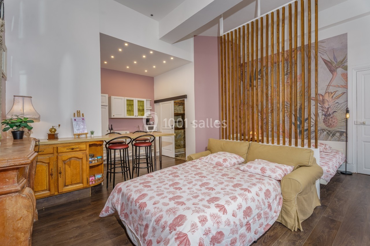 Studio lumineux avec lit double, cuisine équipée, bar avec tabourets, et décoration murale florale.