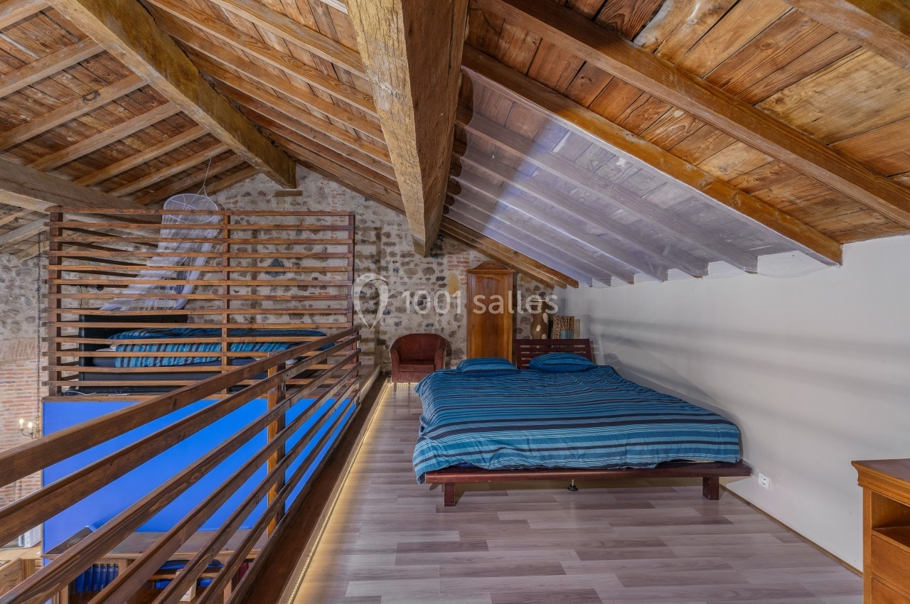 Chambre mansardée avec lit double, plafond en bois, murs en pierre et parquet clair.
