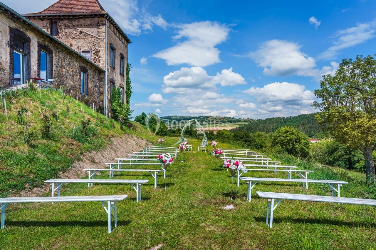 Chaises et bancs blancs disposés en extérieur pour une cérémonie, avec vue sur la campagne et un ciel dégagé.