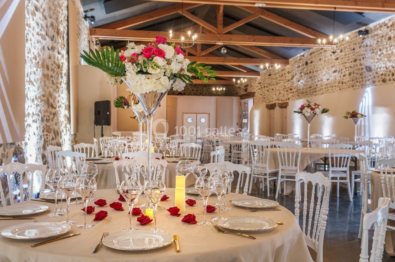 Salle de réception décorée avec des tables rondes, nappes blanches, compositions florales et éclairage chaleureux.