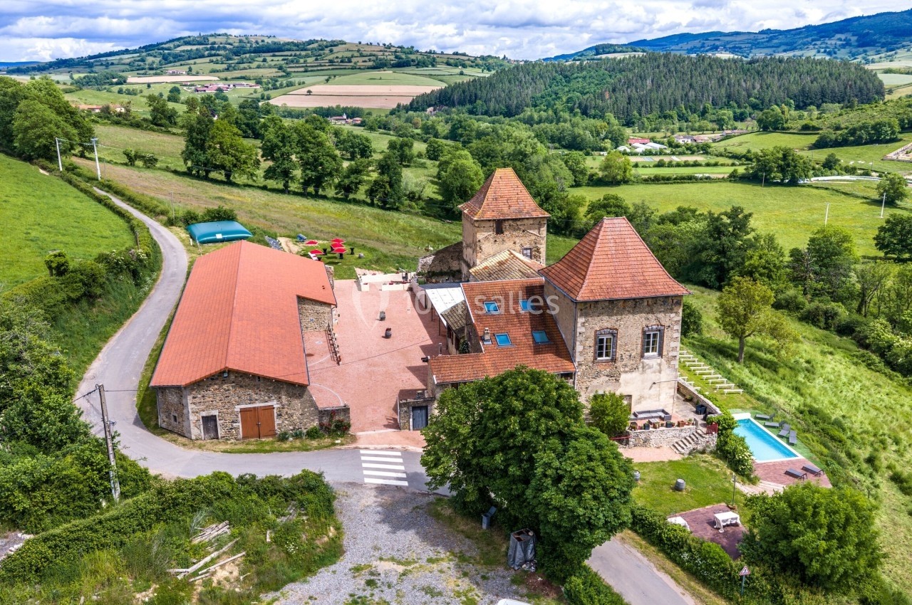 Vue aérienne d'un château historique entouré de bâtiments annexes et de paysages verdoyants en milieu rural.