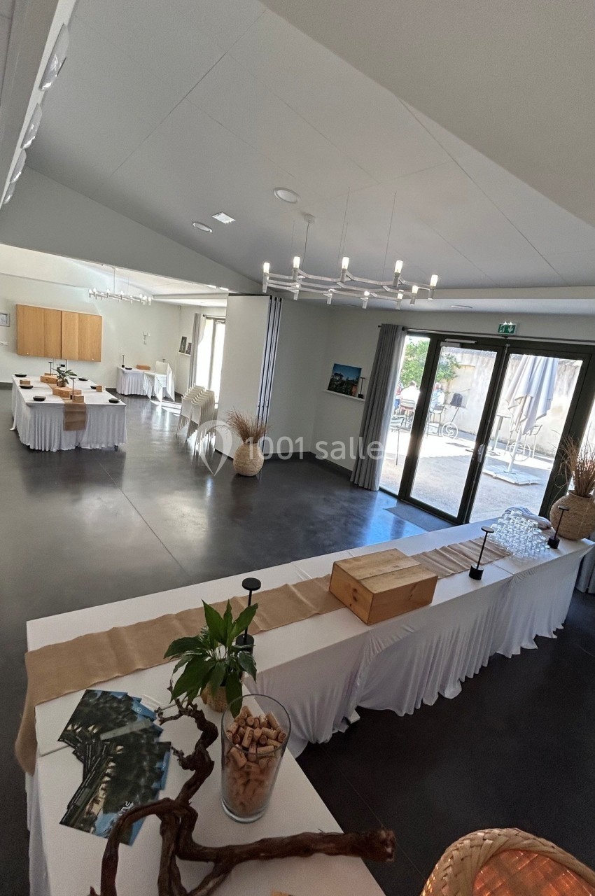 Salle de réception lumineuse avec tables décorées de nappes blanches, vue sur une terrasse extérieure.