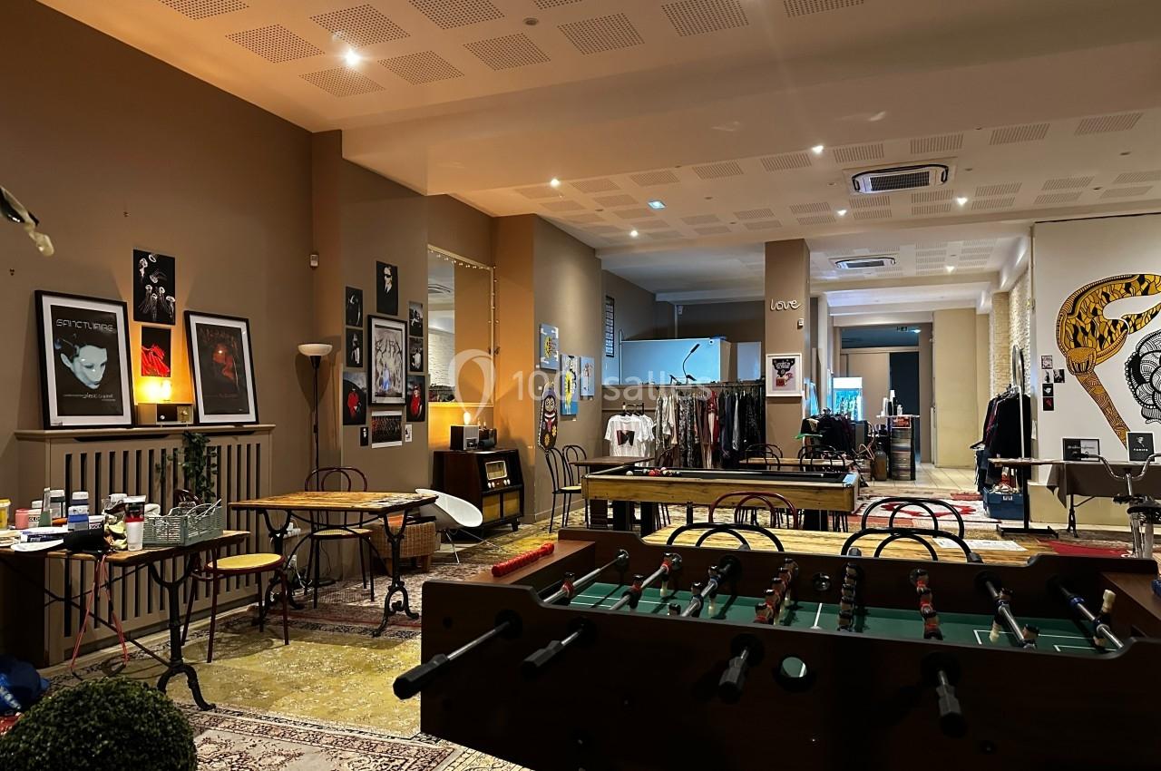 Salle aménagée avec des tables, des chaises, un baby-foot et des affiches décoratives sur les murs.