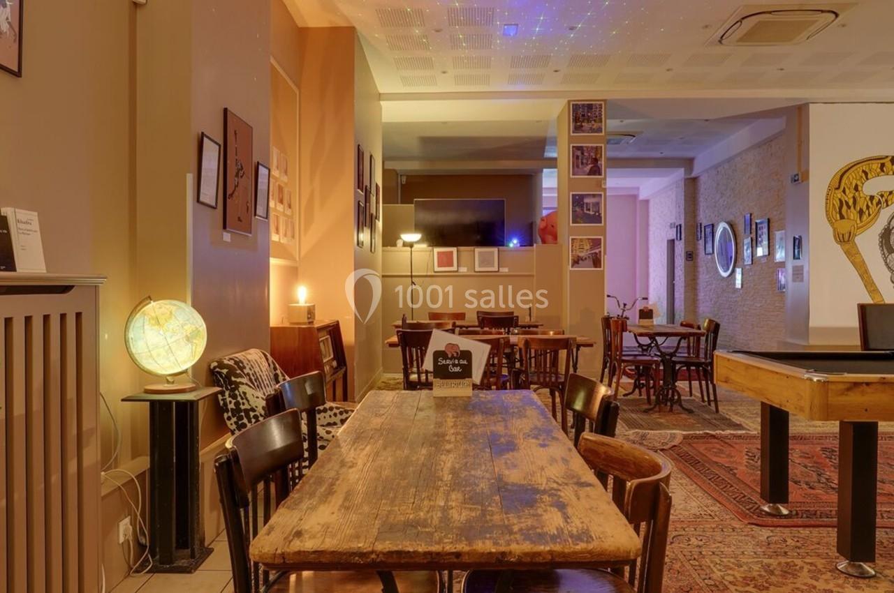 Salle chaleureuse avec tables en bois, chaises assorties, globe lumineux et décoration murale éclectique.