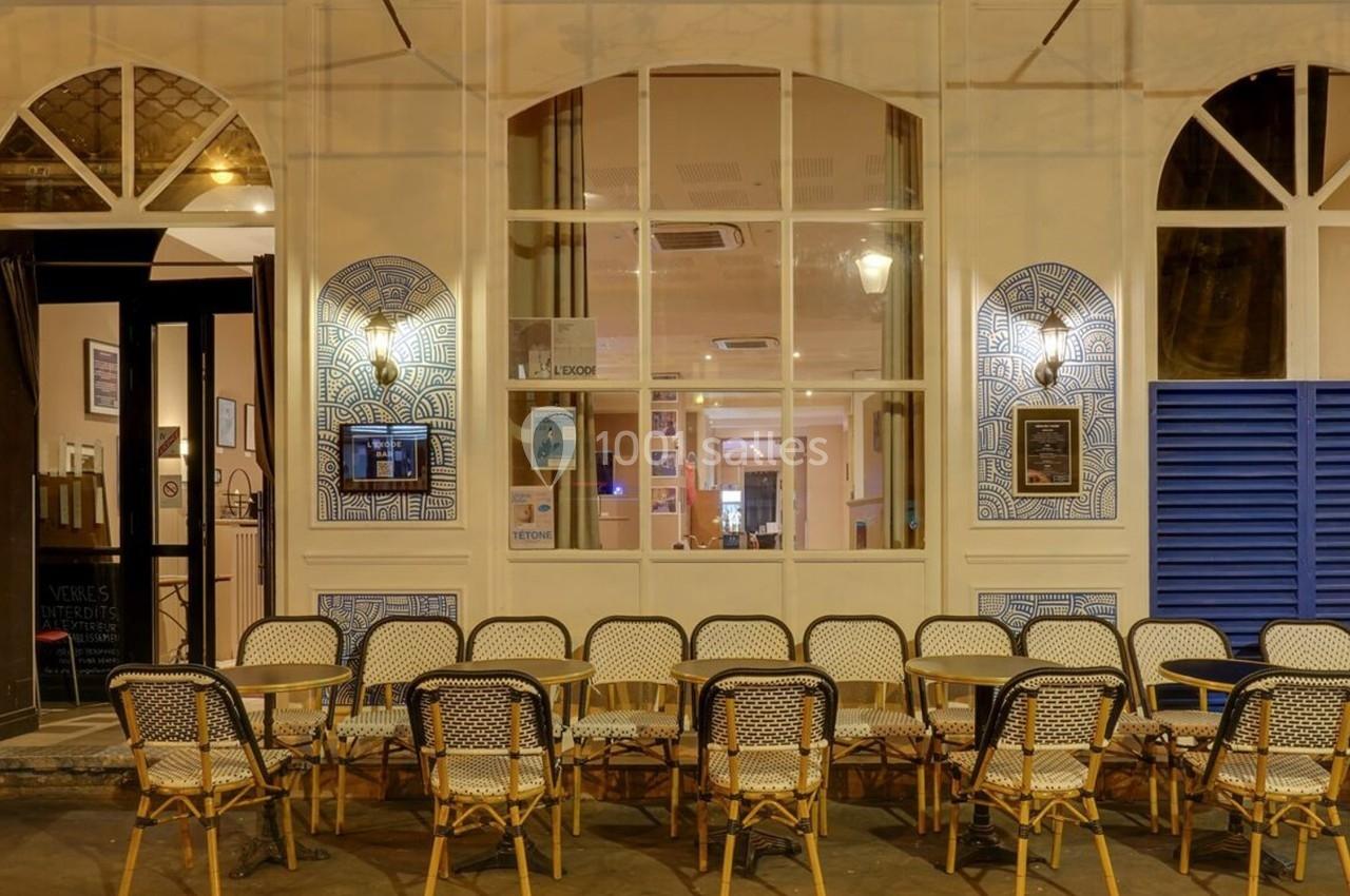 Façade d'un café avec des chaises en osier disposées en rangées devant de grandes fenêtres éclairées.