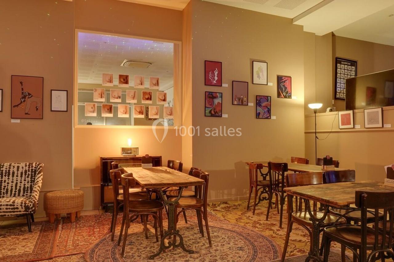 Salle chaleureuse avec tables en bois, chaises vintage, murs décorés de cadres et éclairage tamisé.