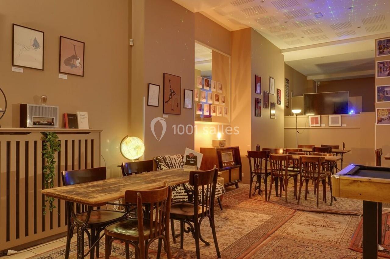 Salle de café chaleureuse avec tables en bois, chaises vintage, décorations murales et éclairage tamisé.