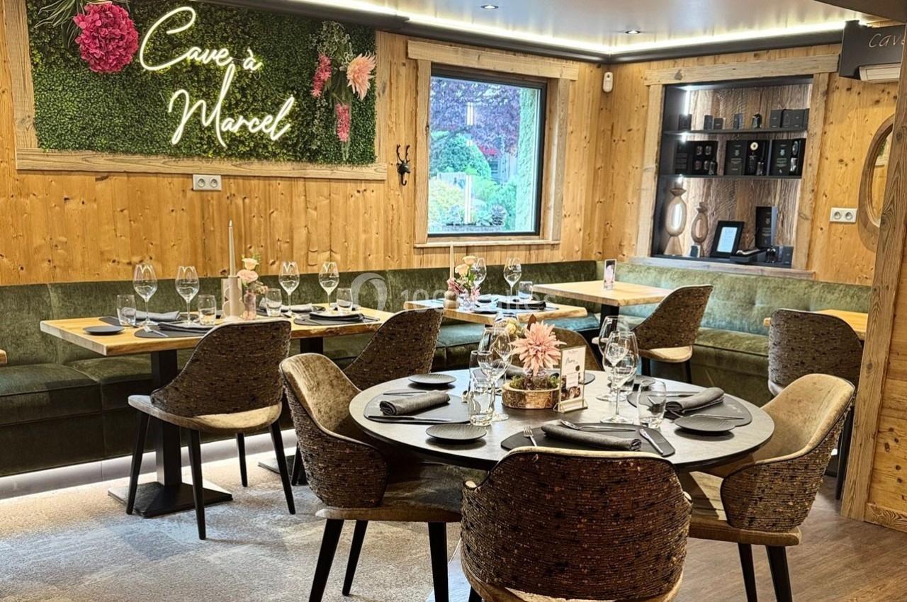 Salle de restaurant chaleureuse avec tables dressées, banquettes en bois et décoration murale végétale éclairée.