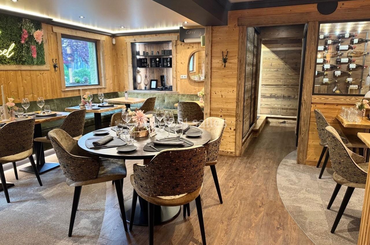 Salle de restaurant chaleureuse avec tables dressées, décoration en bois et lumière naturelle provenant d'une fenêtre.
