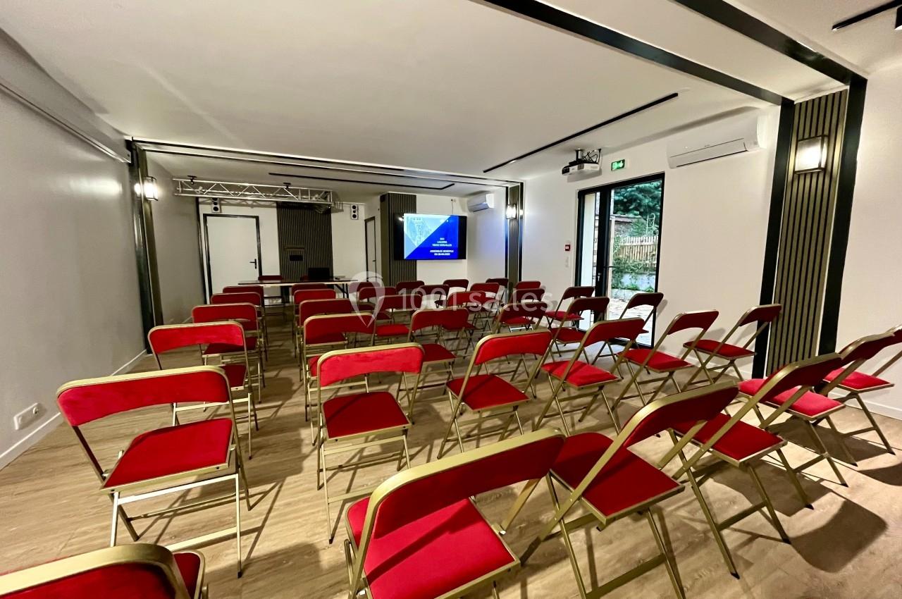 Salle de conférence avec des chaises rouges alignées face à un écran de projection allumé.