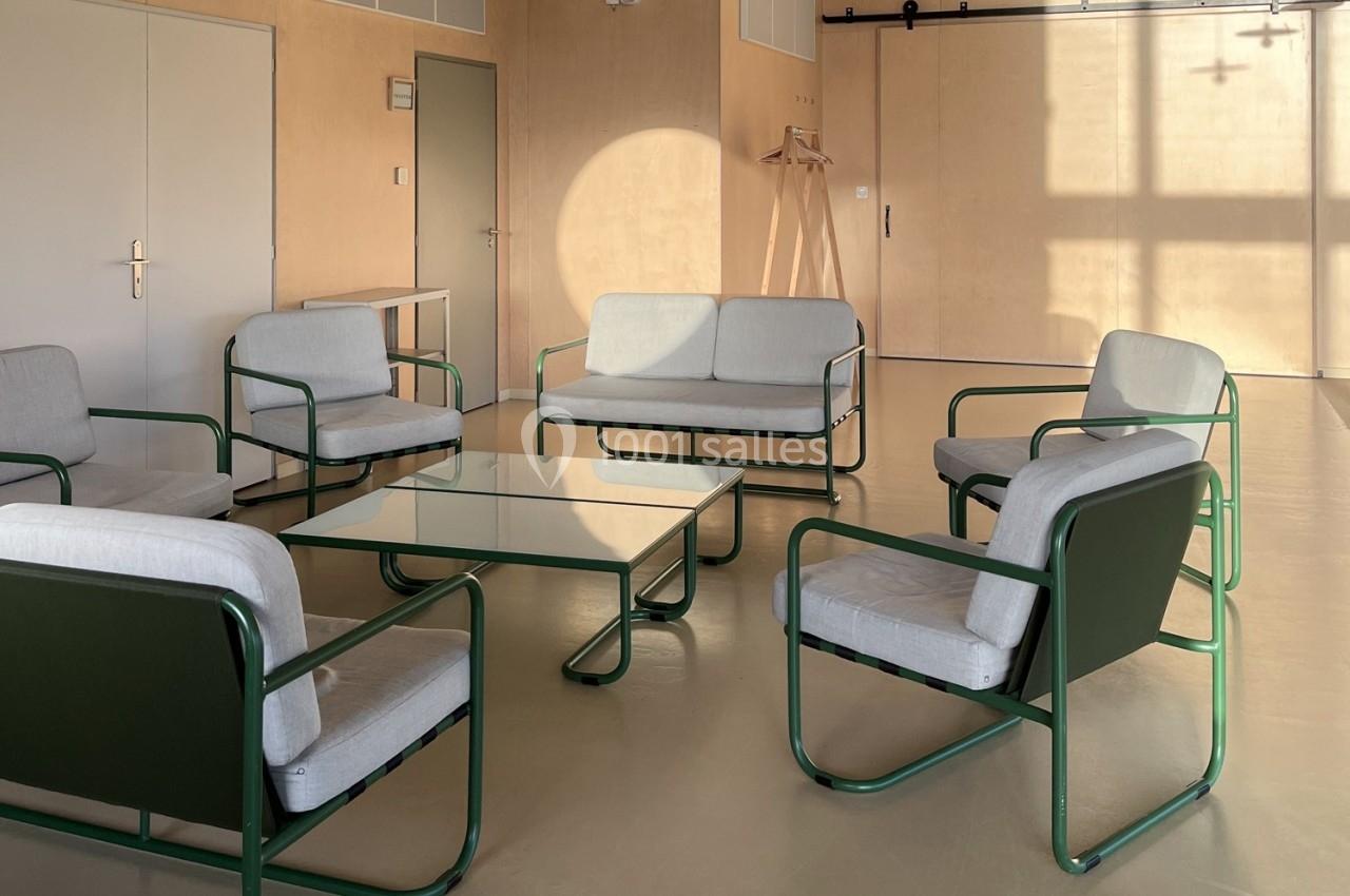 Ensemble de fauteuils et canapé verts avec coussins clairs autour d'une table basse en verre dans une pièce lumineuse.